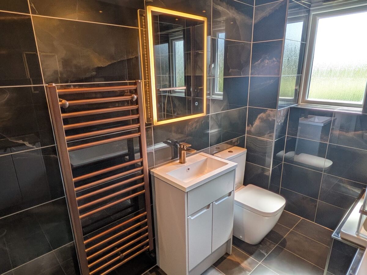 Modern dark tiled bathroom with illuminated mirror and copper heated towel rail