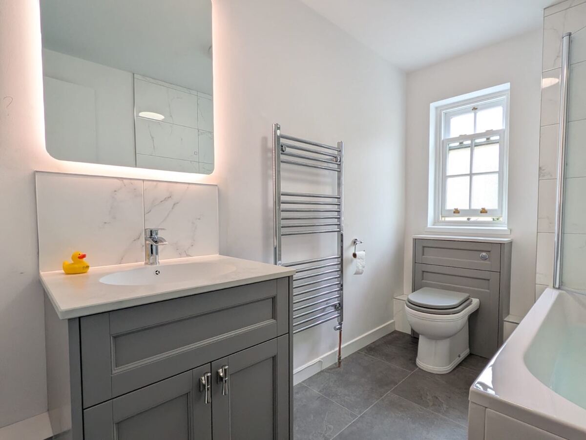 Grey vanity unit with illuminated mirror and marble splashback