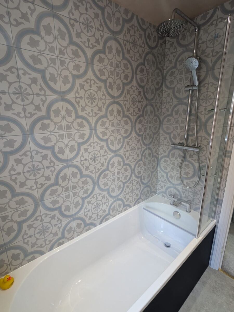 Close-up of bath with rainfall shower and ornate patterned tiles