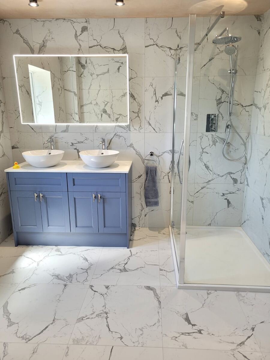 Luxury dual basin vanity in blue with marble-effect tiles and illuminated mirror