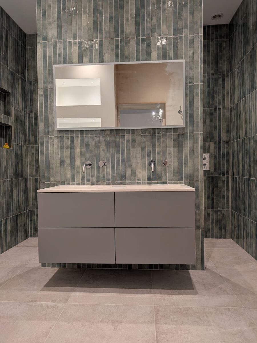 Floating dual vanity with green vertical tiles and wall-mounted taps